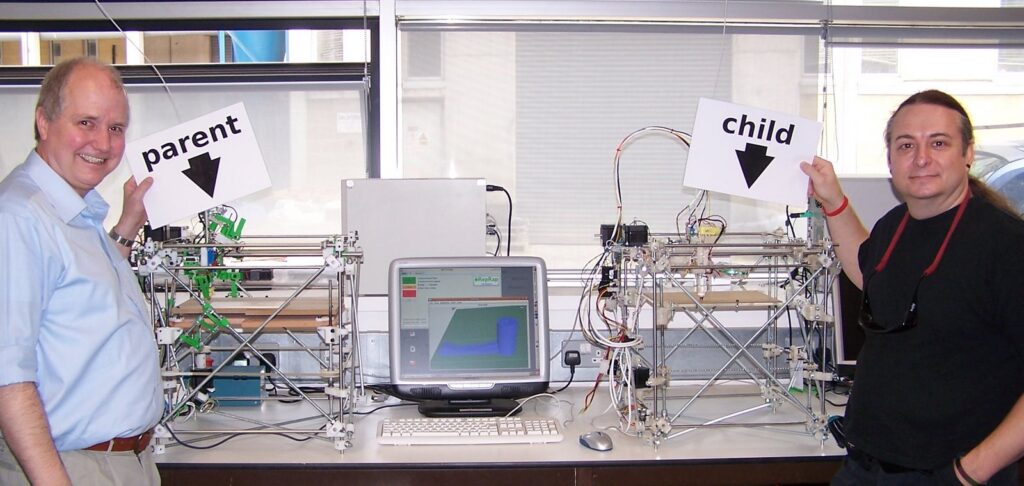 Adrian Bowyer (left) and Vik Olliver (right) with a parent RepRap machine, and the first child machine, made by the RepRap on the left. Image in public domain.
